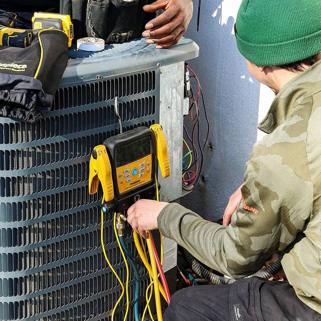 Green Comfort Systems technicians commissioning a heat pump condenser with digital gauges