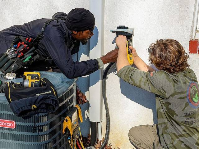 Green Comfort Systems technicians wiring an outdoor condenser disconnect on a Baltimore-area home
